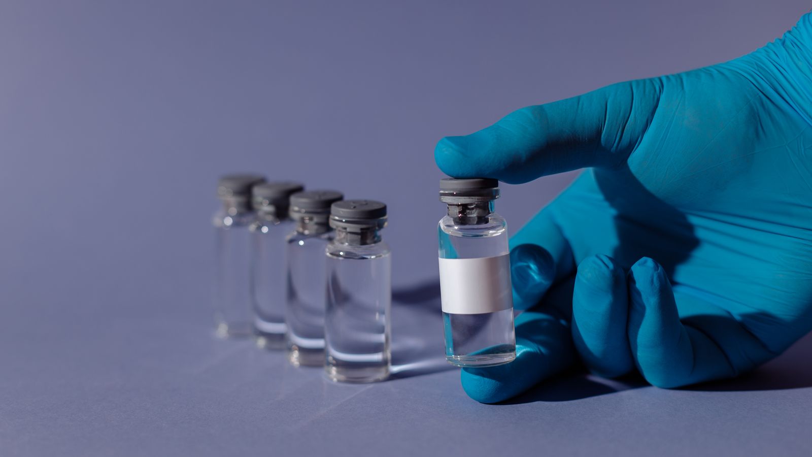 Blue-gloved hand holding a transparent vial filled with liquid.